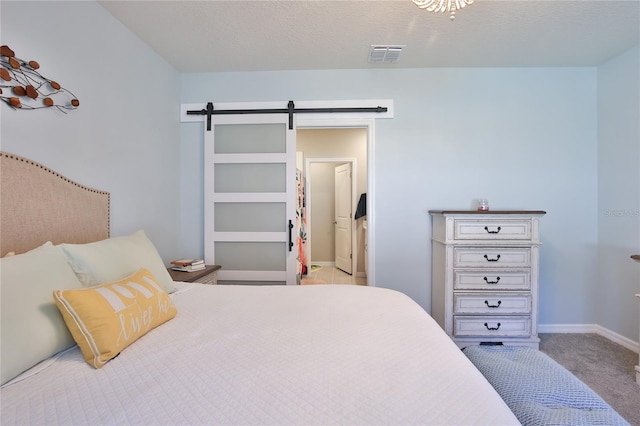 bedroom with carpet floors, visible vents, a textured ceiling, and a barn door