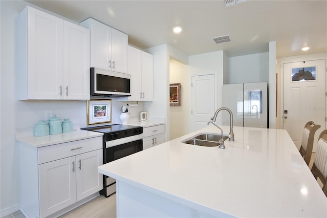 kitchen featuring white microwave, electric range, a sink, visible vents, and a center island with sink