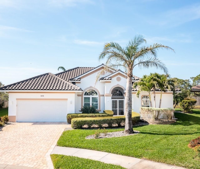 mediterranean / spanish home featuring decorative driveway, a tile roof, stucco siding, an attached garage, and a front lawn