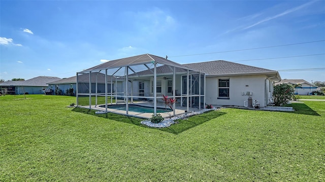 rear view of house with stucco siding, a lawn, a ceiling fan, a lanai, and an outdoor pool