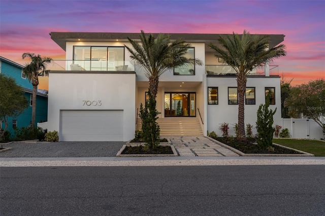 contemporary home featuring a garage, stucco siding, a balcony, and fence