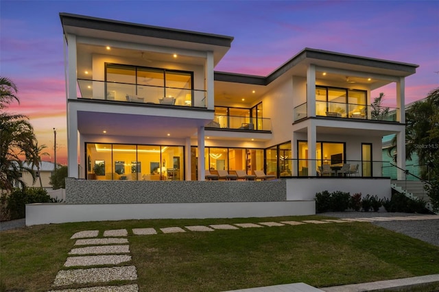 back of house featuring stucco siding, a balcony, and a yard