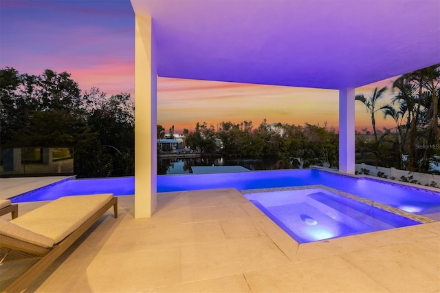 pool at dusk featuring a patio, an in ground hot tub, and an infinity pool