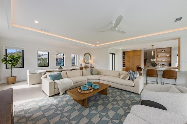 living room with ceiling fan with notable chandelier, a raised ceiling, recessed lighting, and visible vents