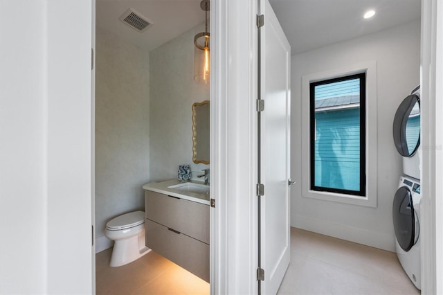 bathroom featuring tile patterned flooring, visible vents, toilet, stacked washer and clothes dryer, and vanity