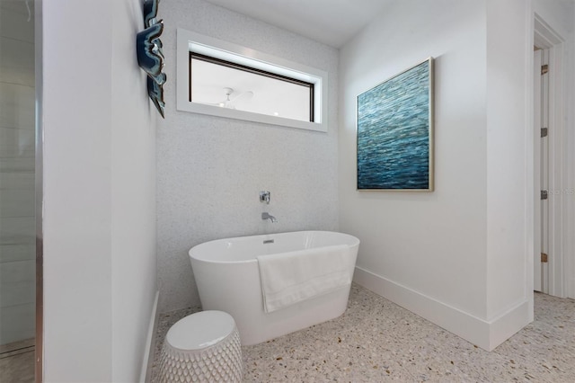 bathroom featuring speckled floor, baseboards, and a freestanding bath