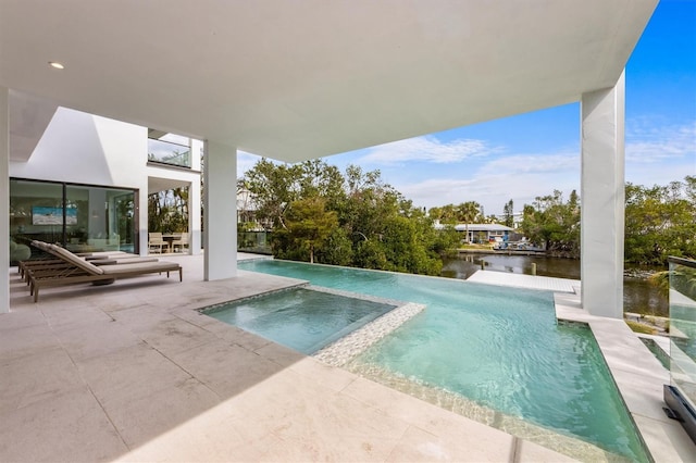 view of swimming pool featuring a patio area, a water view, and a pool with connected hot tub