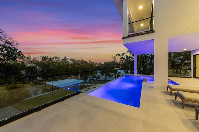 pool at dusk with a patio and an outdoor pool