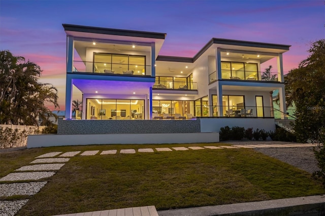 back of house with stucco siding, a balcony, and a lawn