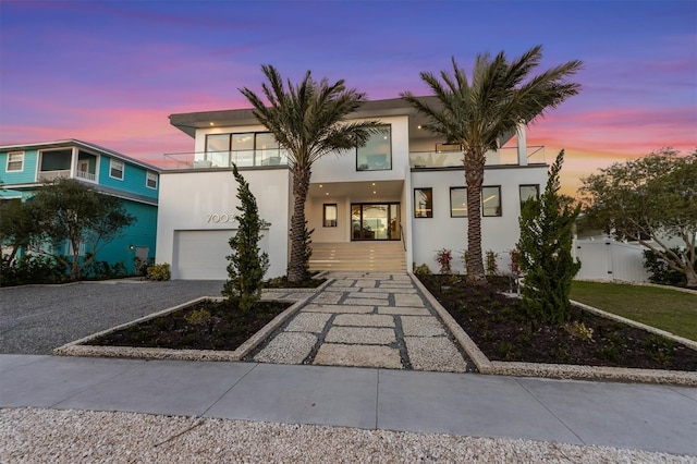 contemporary home featuring stucco siding, decorative driveway, fence, a garage, and a balcony