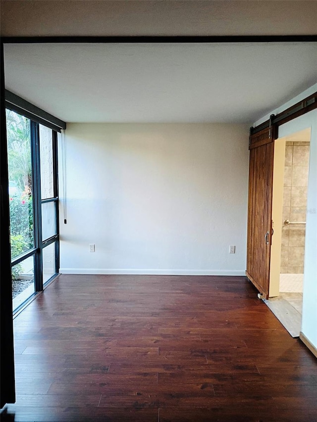 empty room featuring a barn door, dark wood-style flooring, plenty of natural light, and floor to ceiling windows