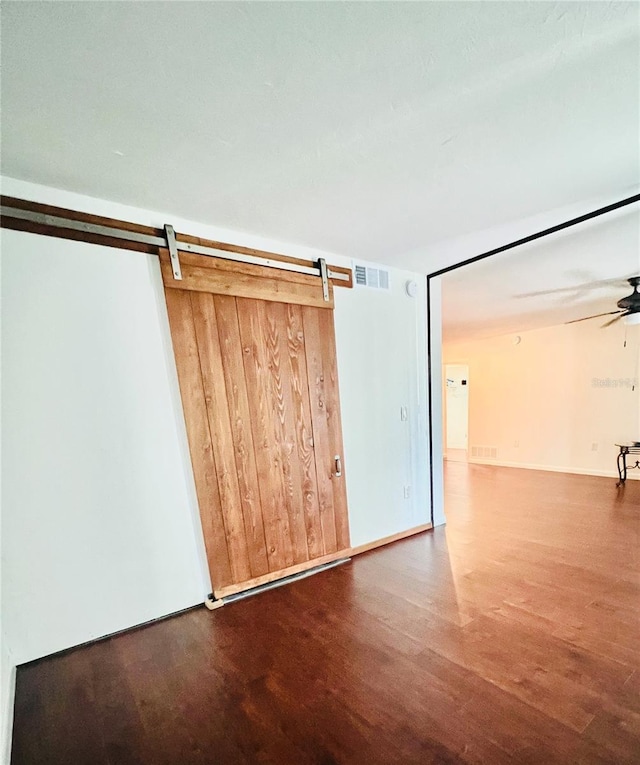 spare room featuring a barn door, visible vents, ceiling fan, and wood finished floors