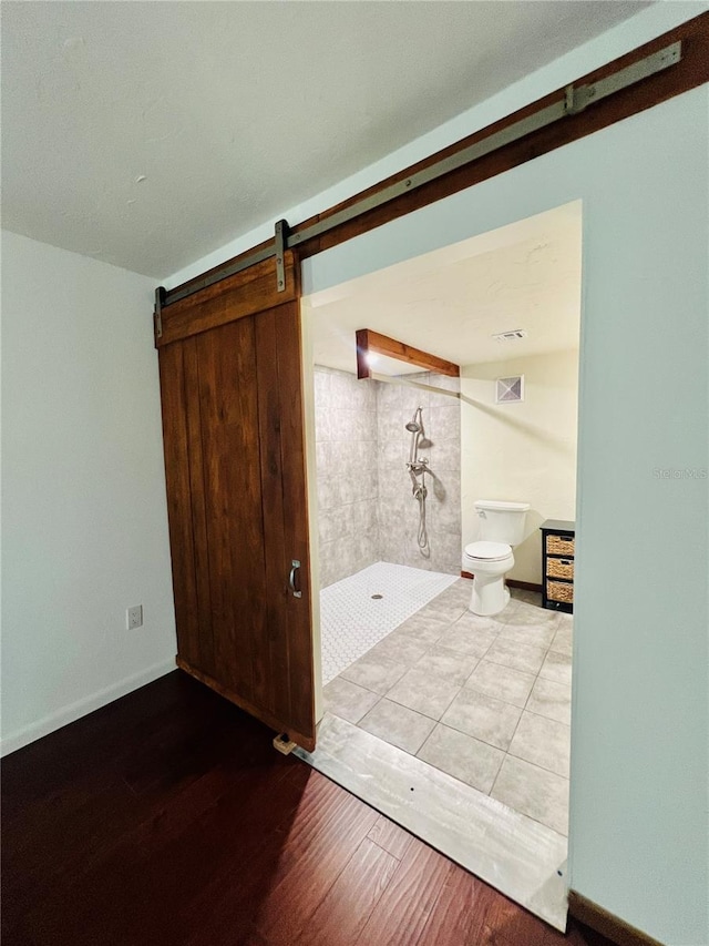 empty room with baseboards, a barn door, visible vents, and wood finished floors