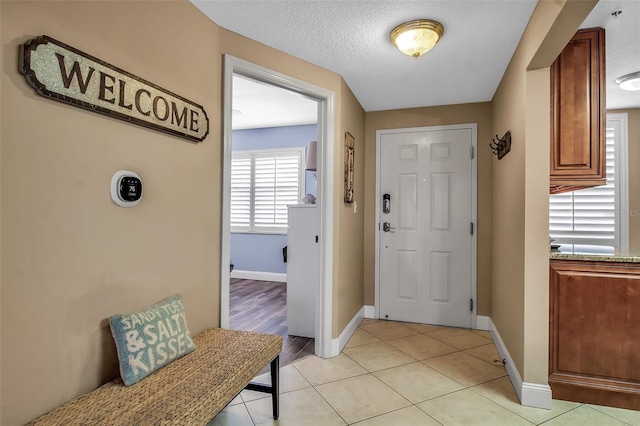 foyer with a textured ceiling, light tile patterned flooring, and baseboards