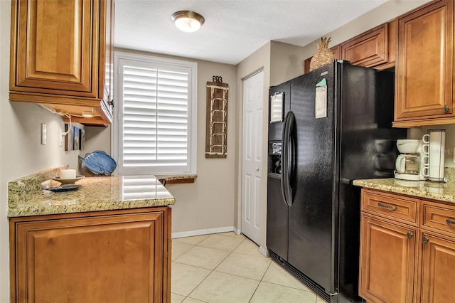 kitchen with light tile patterned floors, light stone counters, brown cabinetry, and black fridge with ice dispenser