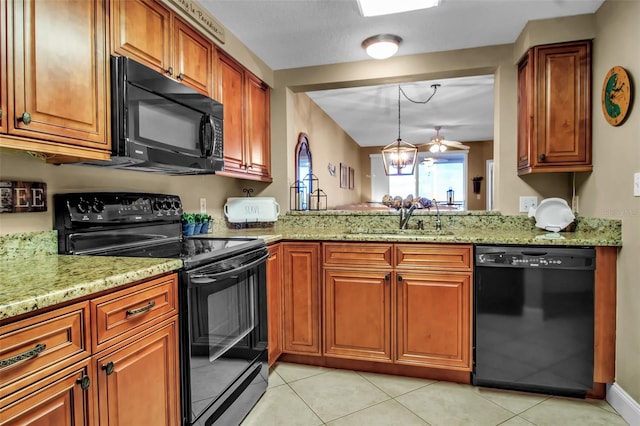 kitchen featuring brown cabinetry, hanging light fixtures, light stone countertops, black appliances, and a sink