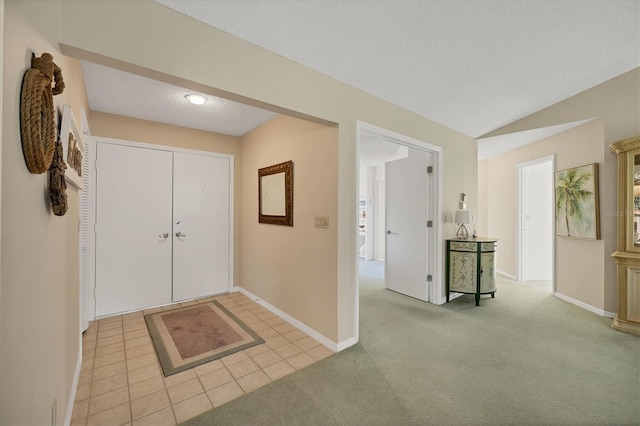 entrance foyer with a textured ceiling, light tile patterned flooring, light colored carpet, baseboards, and vaulted ceiling