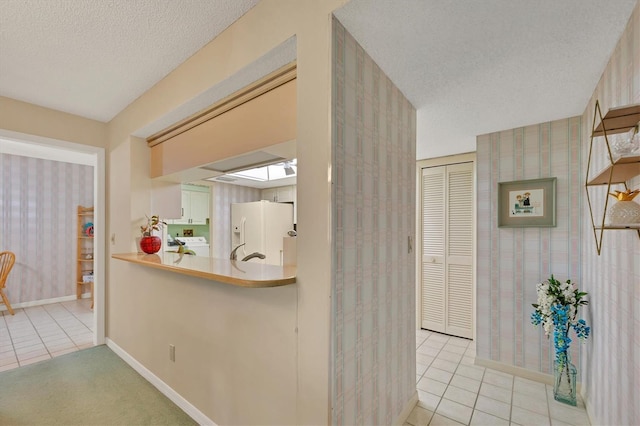 hall featuring a textured ceiling, light tile patterned flooring, baseboards, and wallpapered walls