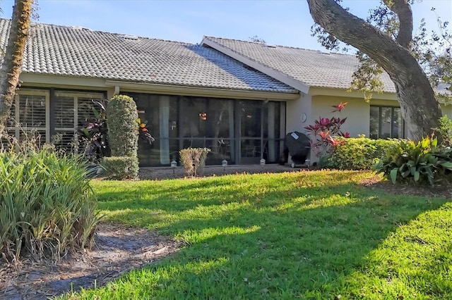 rear view of property featuring a sunroom, stucco siding, a lawn, and a tiled roof