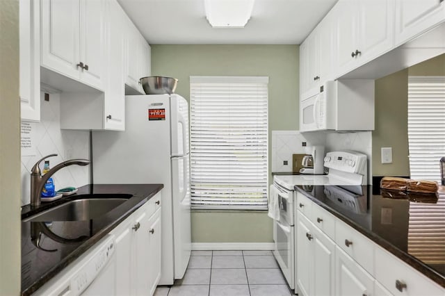 kitchen with light tile patterned floors, white appliances, a sink, white cabinetry, and dark countertops