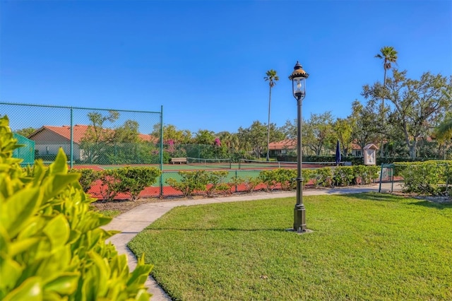 view of community with a tennis court, fence, and a lawn