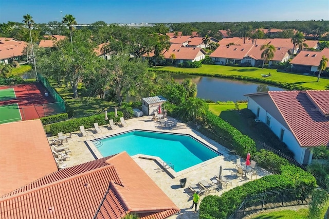 pool with an outbuilding, a water view, a patio area, fence, and a residential view