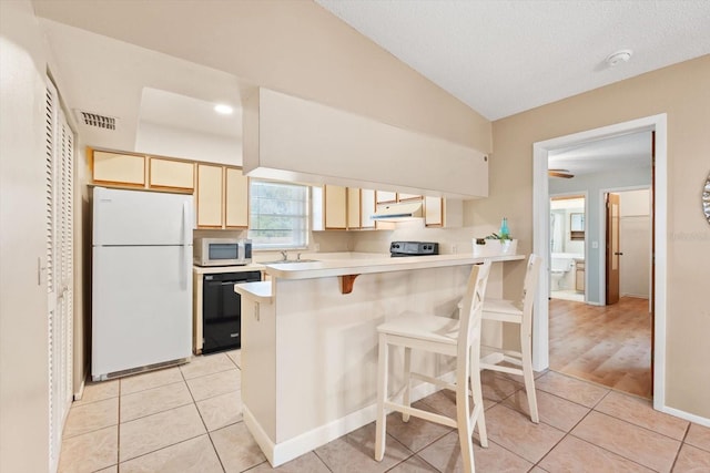 kitchen featuring black dishwasher, visible vents, a breakfast bar area, freestanding refrigerator, and light countertops