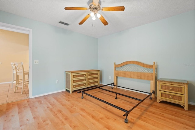 bedroom featuring visible vents, a textured ceiling, baseboards, and wood finished floors