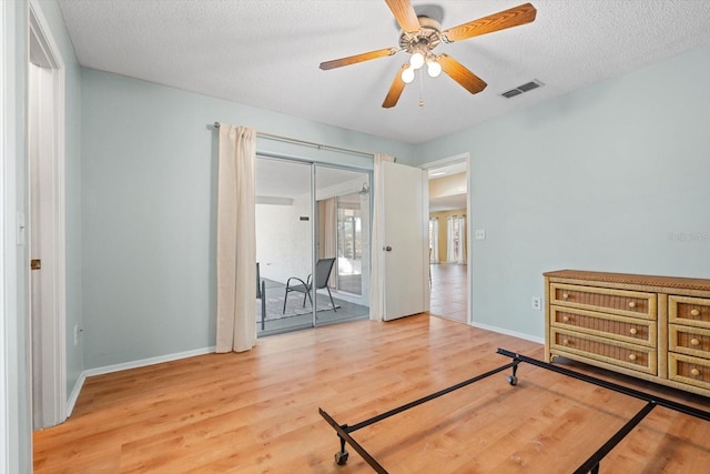 bedroom with a textured ceiling, wood finished floors, visible vents, baseboards, and access to outside