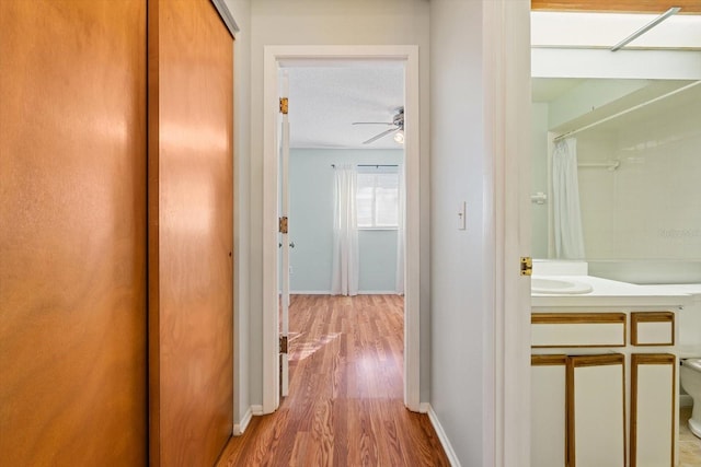 hallway with light wood-style floors, a textured ceiling, and baseboards