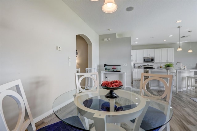 dining room featuring arched walkways, baseboards, visible vents, and light wood finished floors