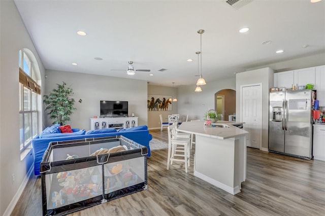 kitchen with arched walkways, a kitchen island, white cabinetry, hanging light fixtures, and stainless steel fridge