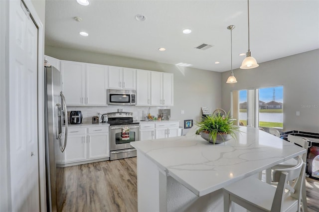 kitchen with visible vents, white cabinets, hanging light fixtures, light stone countertops, and stainless steel appliances