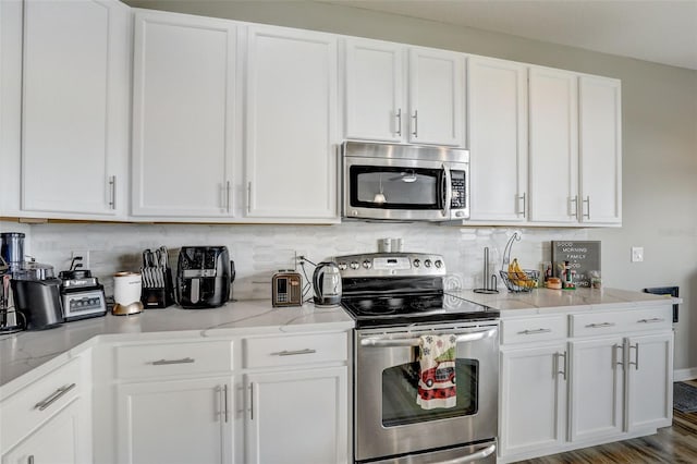 kitchen featuring stainless steel appliances, light stone counters, decorative backsplash, and white cabinets