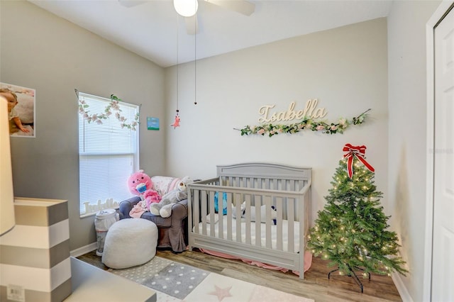 bedroom featuring a crib, ceiling fan, baseboards, and wood finished floors