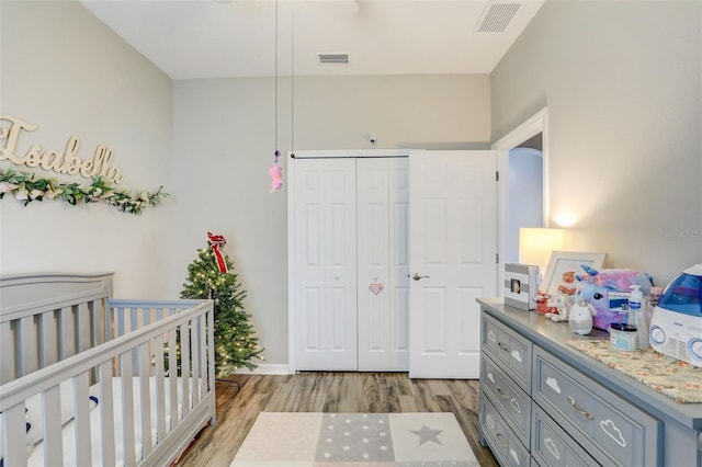 bedroom with a nursery area, light wood finished floors, a closet, and visible vents