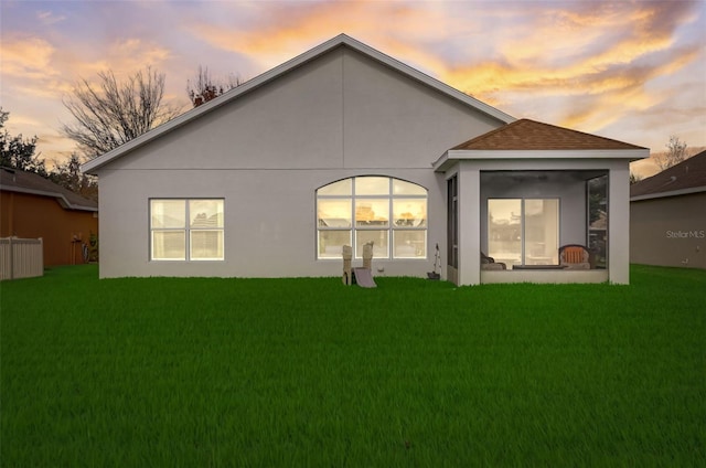 back of property at dusk with roof with shingles, a lawn, a sunroom, and stucco siding