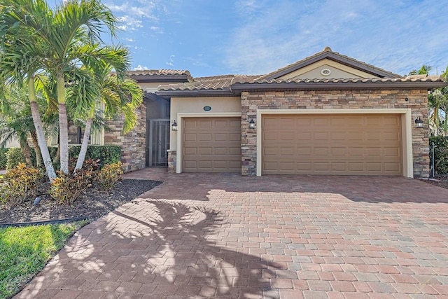 view of front of house featuring stone siding, a tiled roof, an attached garage, decorative driveway, and stucco siding