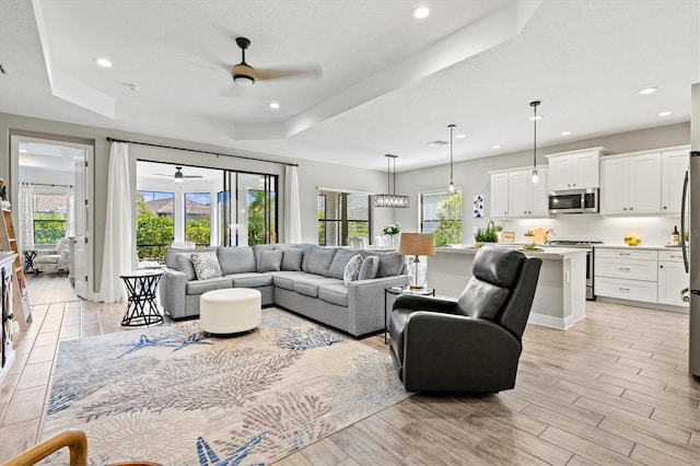 living area featuring light wood-type flooring, a healthy amount of sunlight, a tray ceiling, and a ceiling fan