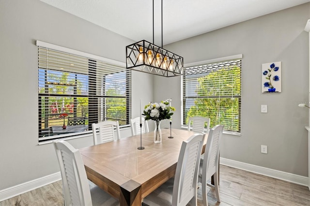 dining area featuring baseboards, light wood finished floors, and an inviting chandelier