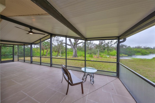 unfurnished sunroom featuring vaulted ceiling with beams, a water view, a wealth of natural light, and a ceiling fan