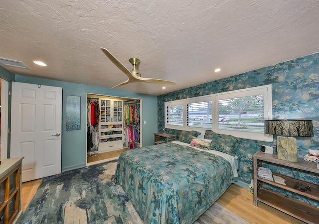 bedroom with a closet, visible vents, a textured ceiling, wood finished floors, and wallpapered walls