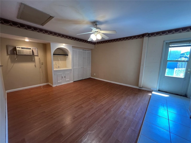 interior space featuring a wall unit AC, wood finished floors, a ceiling fan, and baseboards