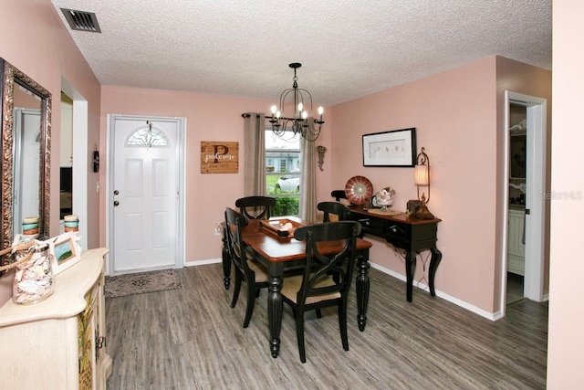 dining room with baseboards, visible vents, wood finished floors, a textured ceiling, and a notable chandelier