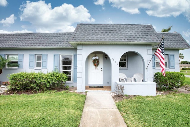 view of front of home with stucco siding, a front lawn, mansard roof, and roof with shingles