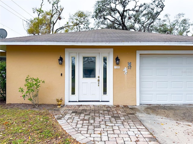 entrance to property featuring a garage, a shingled roof, and stucco siding