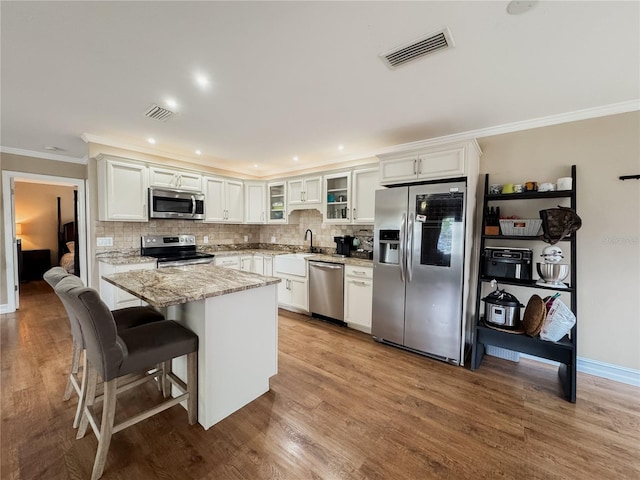 kitchen with visible vents, white cabinetry, appliances with stainless steel finishes, light stone countertops, and glass insert cabinets