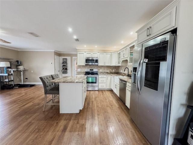 kitchen with stainless steel appliances, glass insert cabinets, white cabinetry, a kitchen island, and light stone countertops