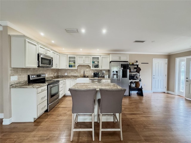 kitchen featuring a center island, white cabinetry, appliances with stainless steel finishes, light stone countertops, and glass insert cabinets