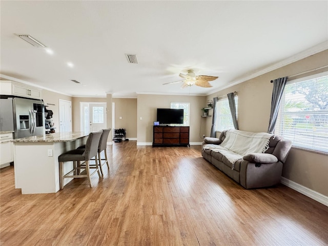 living room with ornamental molding, visible vents, and light wood-style flooring